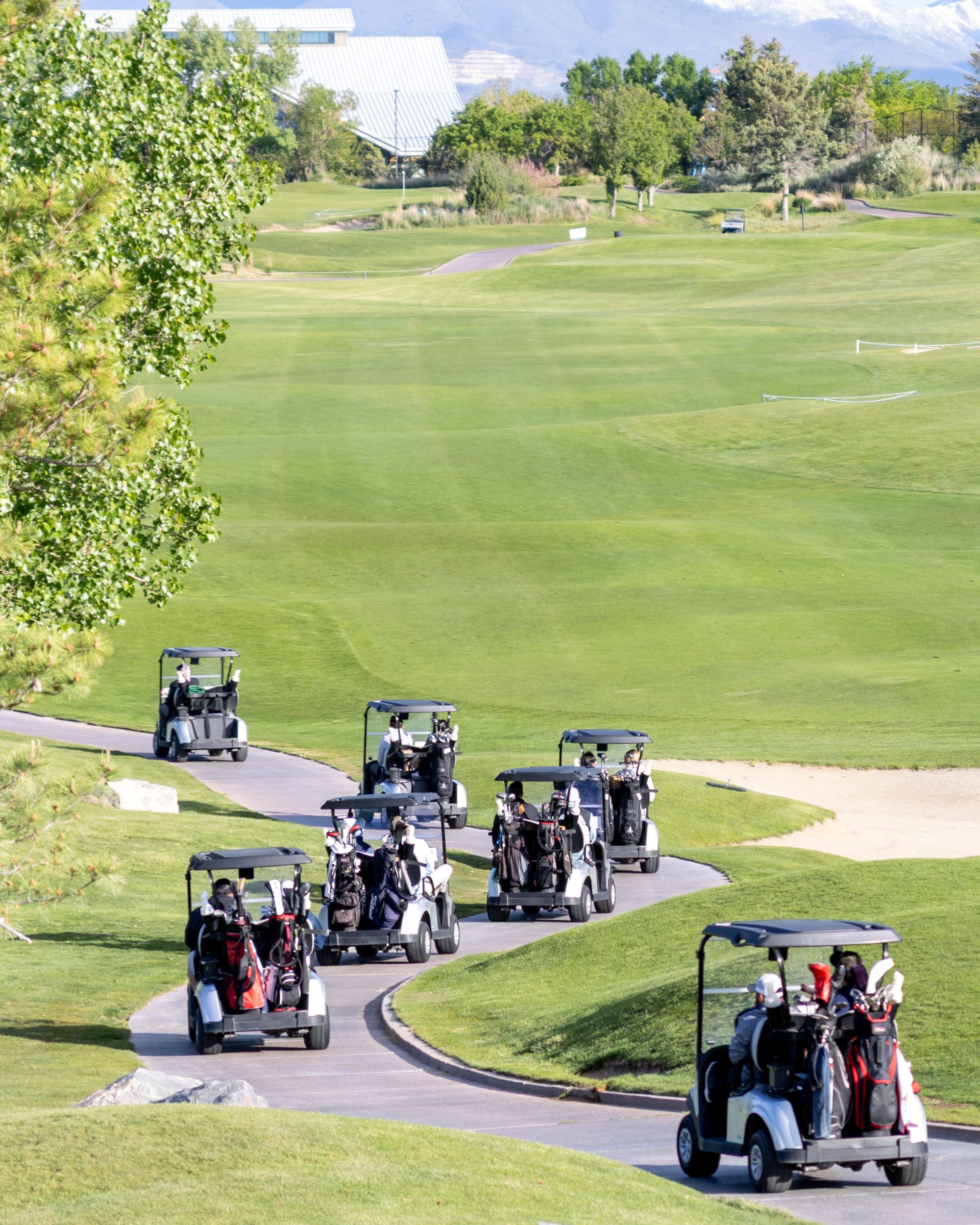 A fleet of golf carts loaded with bags winding down the cart path on a lush green fairway