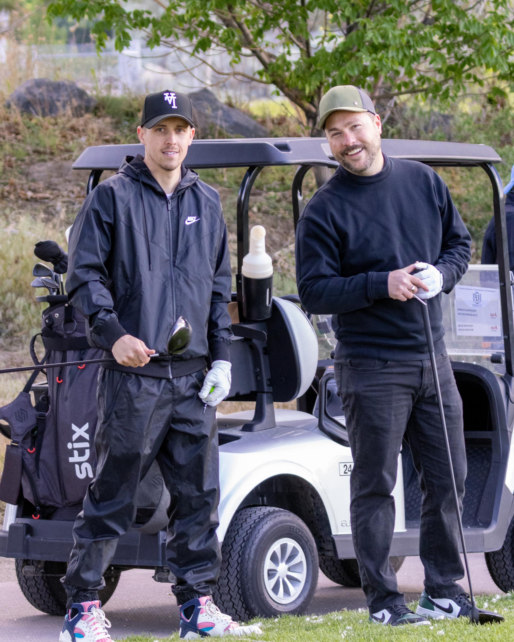 Two golfers standing beside their cart on the fairway, holding clubs and smiling at the camera