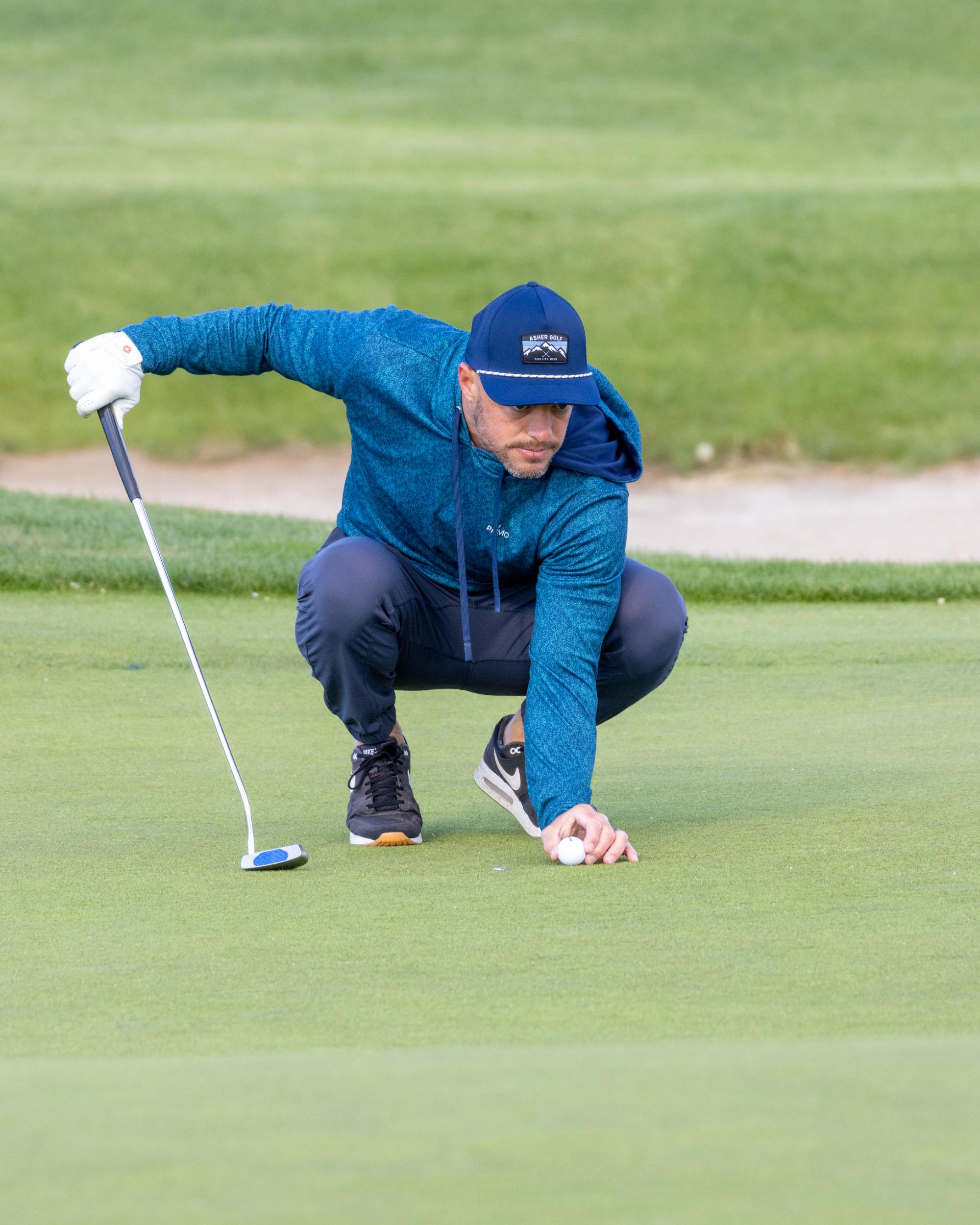 Golfer crouching on the putting green to line up his ball before taking a putt