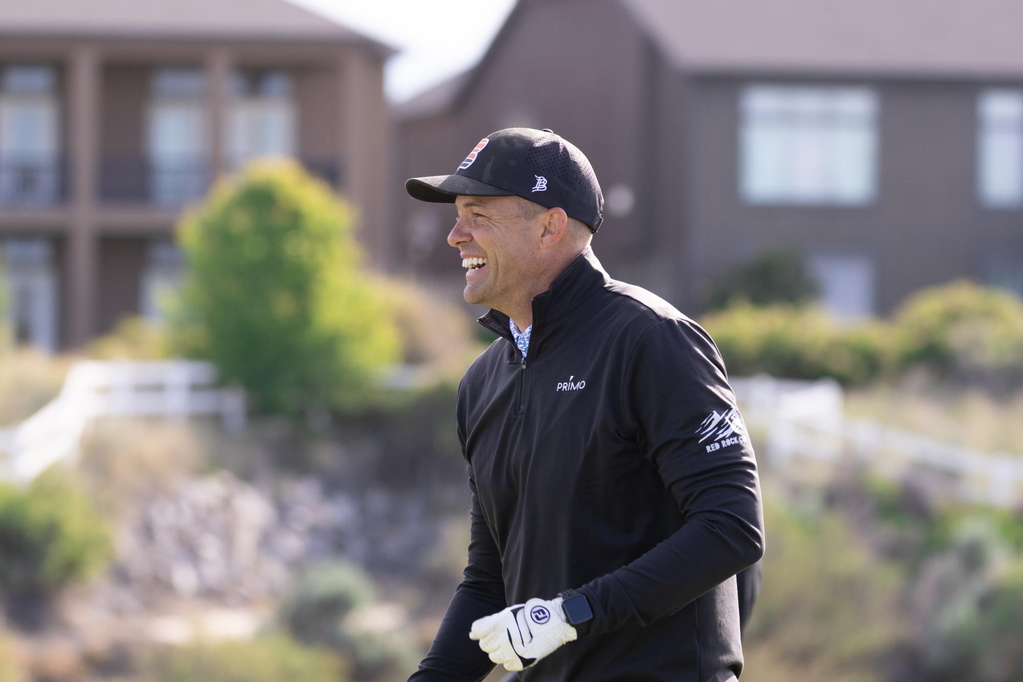 Player in black cap and jacket laughing on the fairway, enjoying a light moment during play