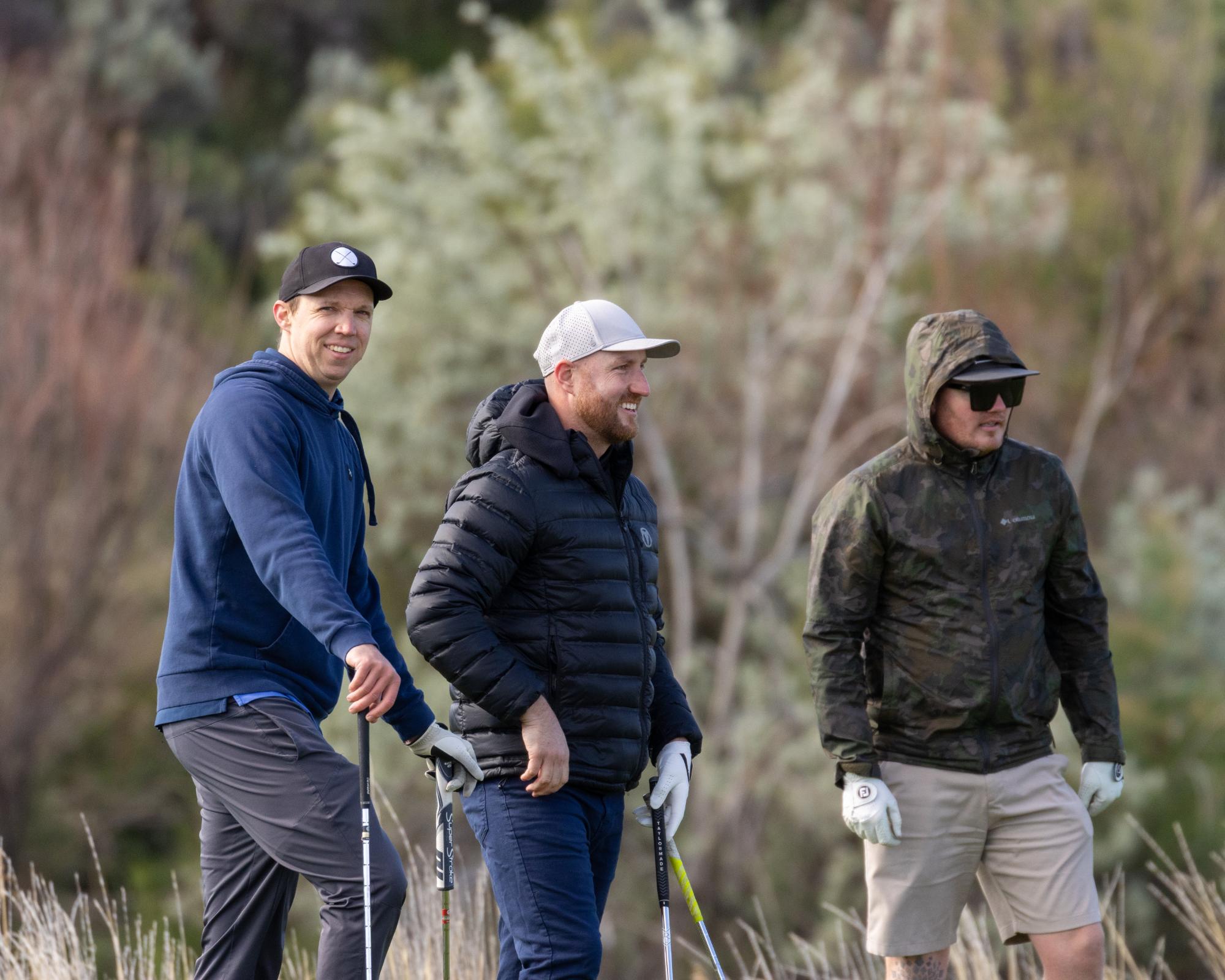 Three golfers standing at the edge of the rough, holding clubs and surveying their next shot