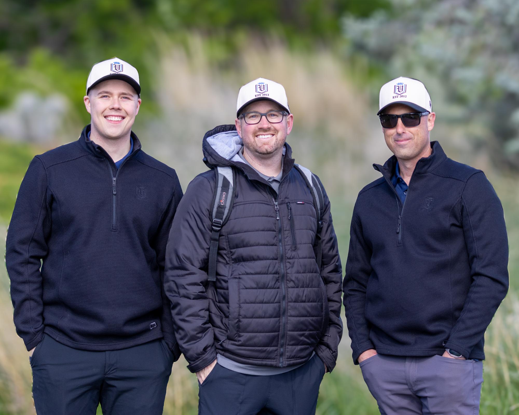 Tournament organizers in branded caps standing side by side, smiling against a backdrop of course greenery