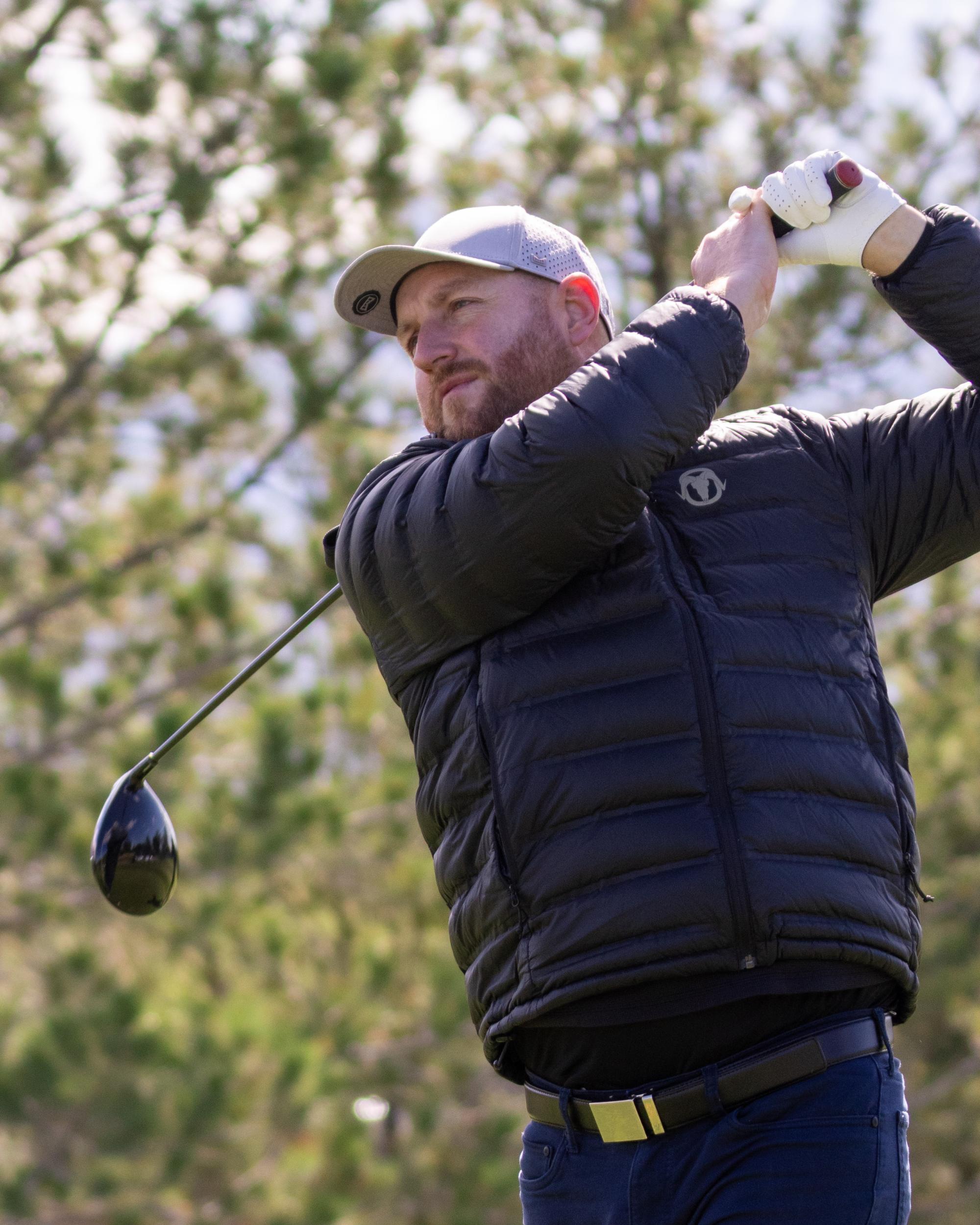 Golfer in a gray cap swinging a driver, focused on his follow-through at the tee