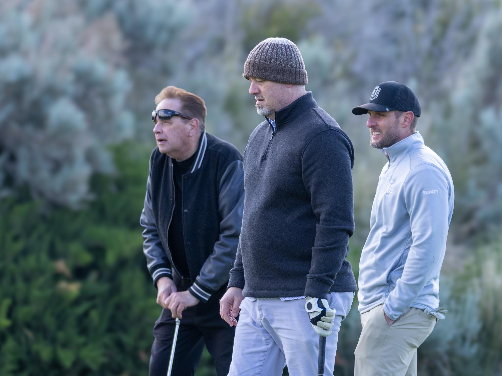 Three players lining up beside the green, concentrating on ball position before taking their shot